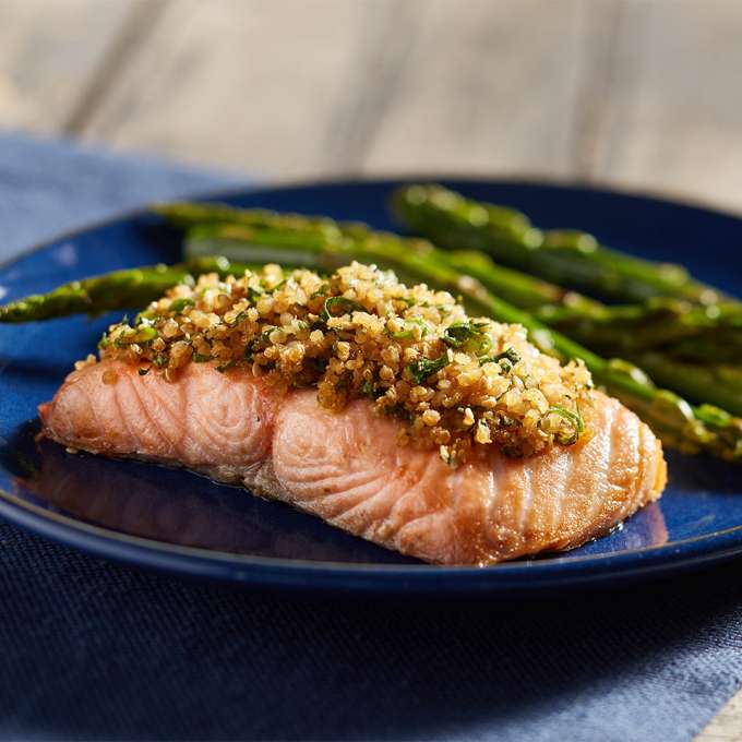 A dark blue plate on a wooden table holds a serving of Manuka Honey & Sesame Ginger-Crusted Salmon