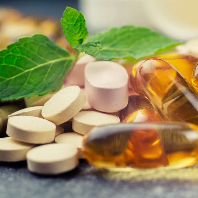 Several pills of different colors and yellow gel capsules sit next to each other on a black counter.