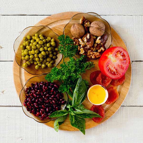 A wooden plate on a white wooden table holding glass bowls with different beans and nuts in them. A 