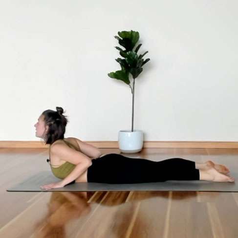 presenting as woman laying on stomach on a mat in black yoga pants with sports top with upper body raised up