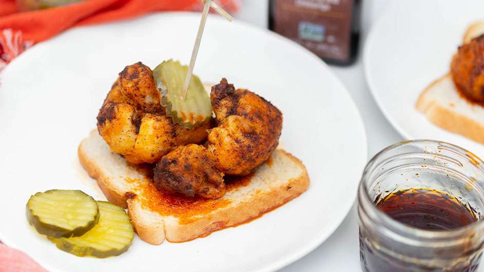 Nashville hot fried cauliflower on top of a slice of white bread with pickles around