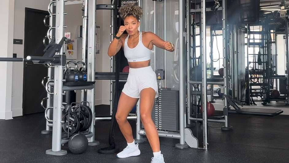 Monica Jones in a gym wearing white workout clothes punching the air