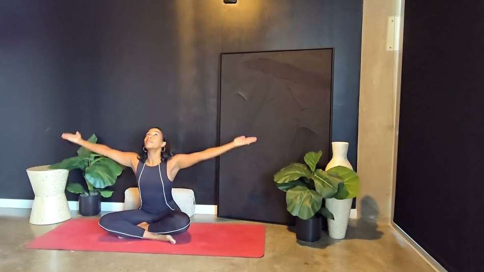 Georgette Dunn sitting on a red yoga mat with her arms up and outwards above her head