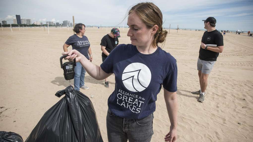 light skinned female presenting person weighing a trash bag on a beach after cleanup